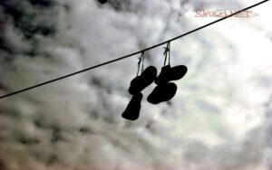 Schuhe hängen auf Stromkabel im grauen Himmel.